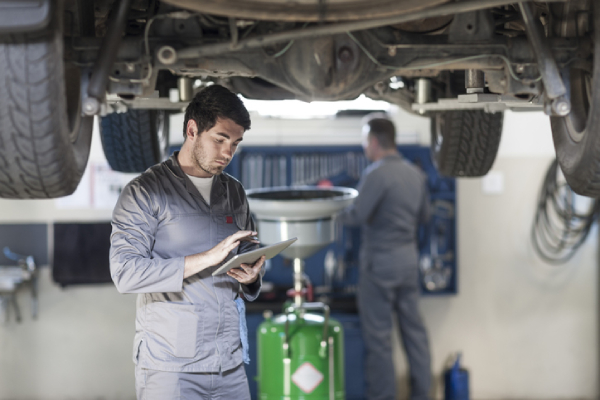 Technician under vehicle reviewing tablet information