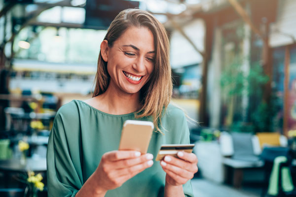 Woman smiling at mobile phone, holding debit card