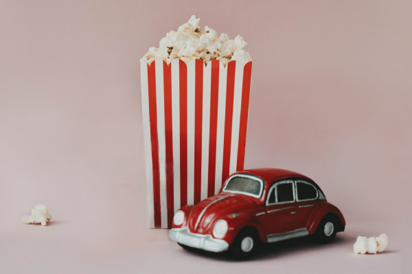 red toy car next to a bucket of popcorn with pale pink background