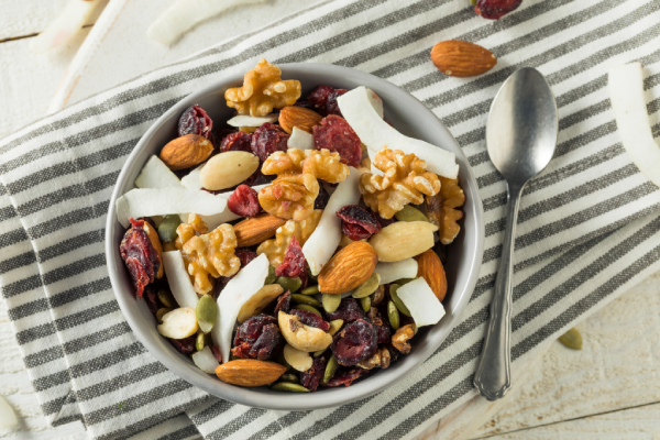 bowl of trail mix with walnuts, almonds, and dried fruits next to a spoon